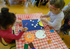 Dzieci dekorują pracę, naklejają kolorowe elementy papierowe.